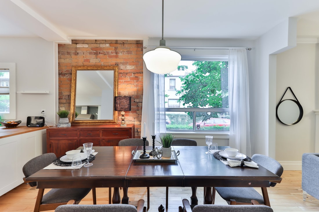 A dark timber dining table set for a meal, in front of an exposed brick chimney breast.