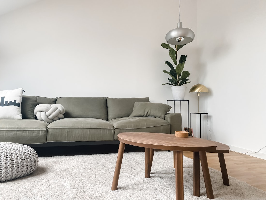 An olive linen sofa beside a walnut oval coffee table in a bright living room.