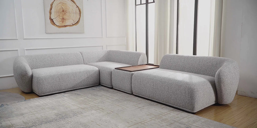 A grey boucle modular sofa with a walnut tray set into it, in a bright room with timber floors.