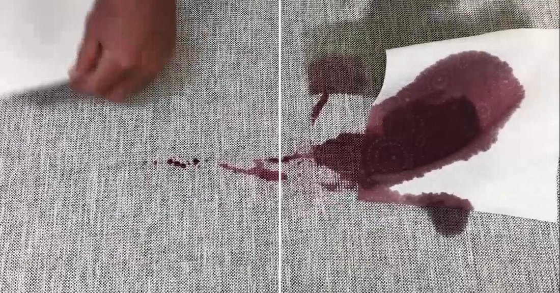A flat panel of grey woven upholstery divided down the middle, with red wine spilled across the join. On the left it beads on the surface and lifts onto a cloth; on the right it has soaked into the weave and spread.