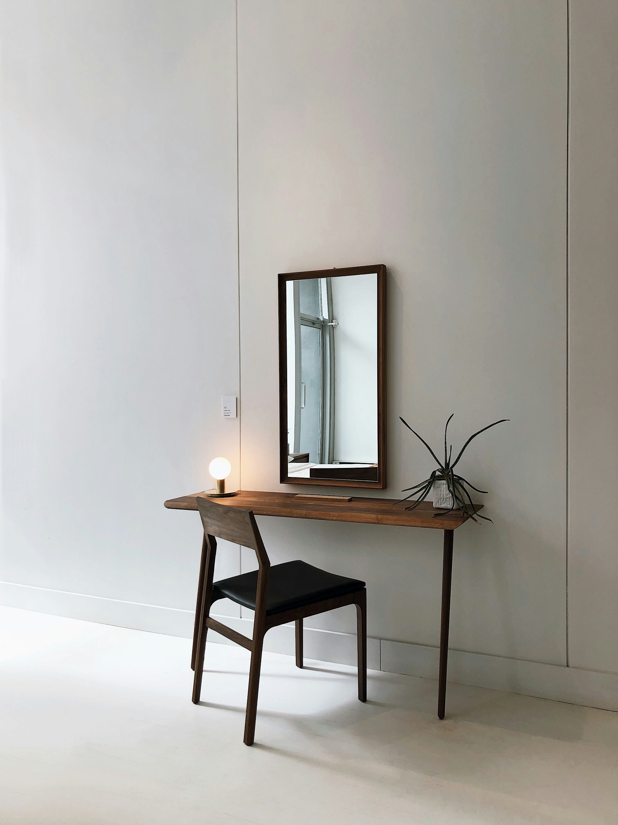 A slim walnut console table and a matching chair beneath a walnut-framed mirror, against a pale wall.